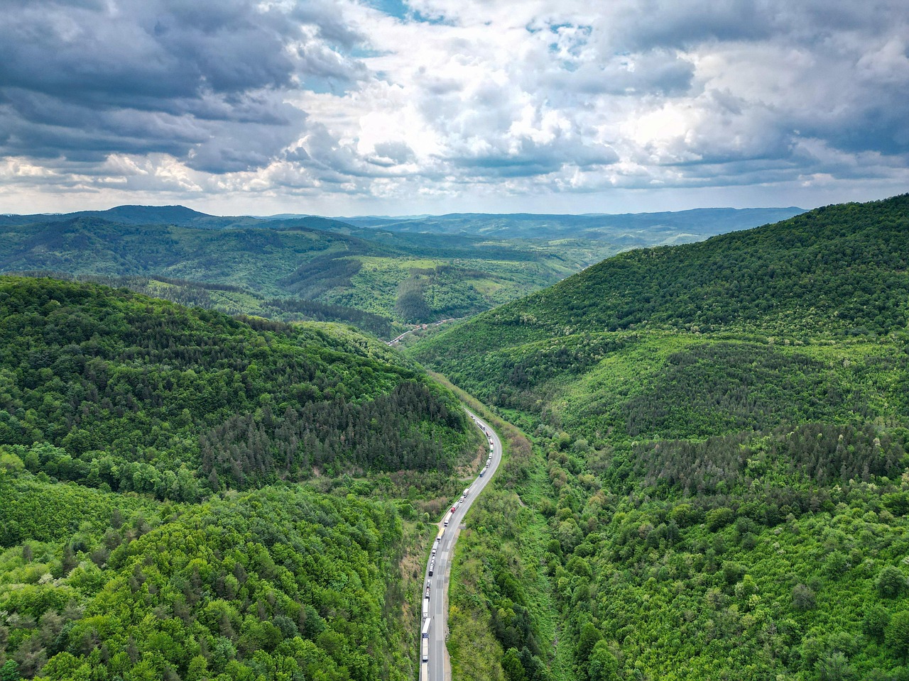 A road winding through a broad forested valley under heavy cloud