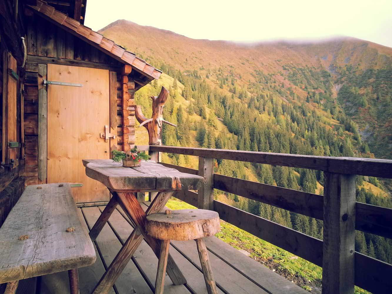 A timber mountain hut with a table and bench overlooking a forested valley